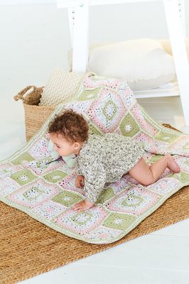 A baby is crawling on a crocheted blanket, made up of green, pink and white squares.