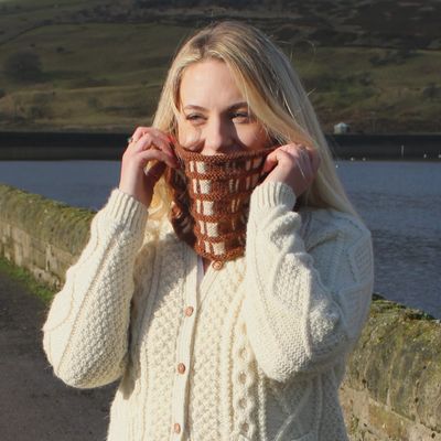 A woman is wearing a brown and cream checked effect knitted cowl.