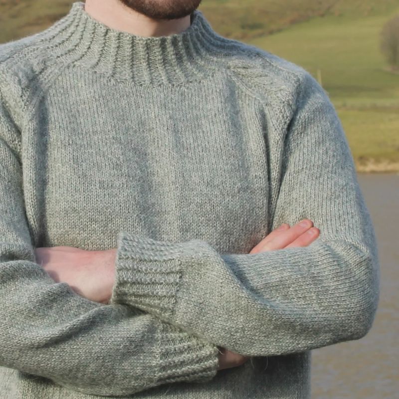 A man is wearing a light grey knitted sweater.
