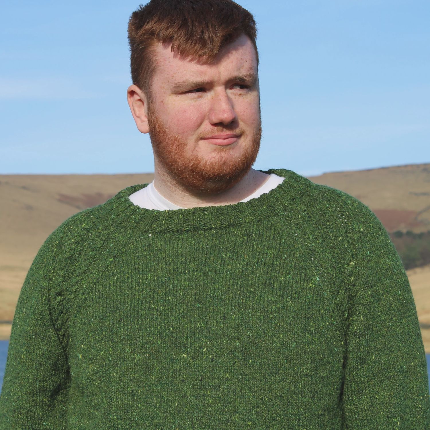 A man is wearing a dark green knitted sweater with cable at the top of the sleeves.