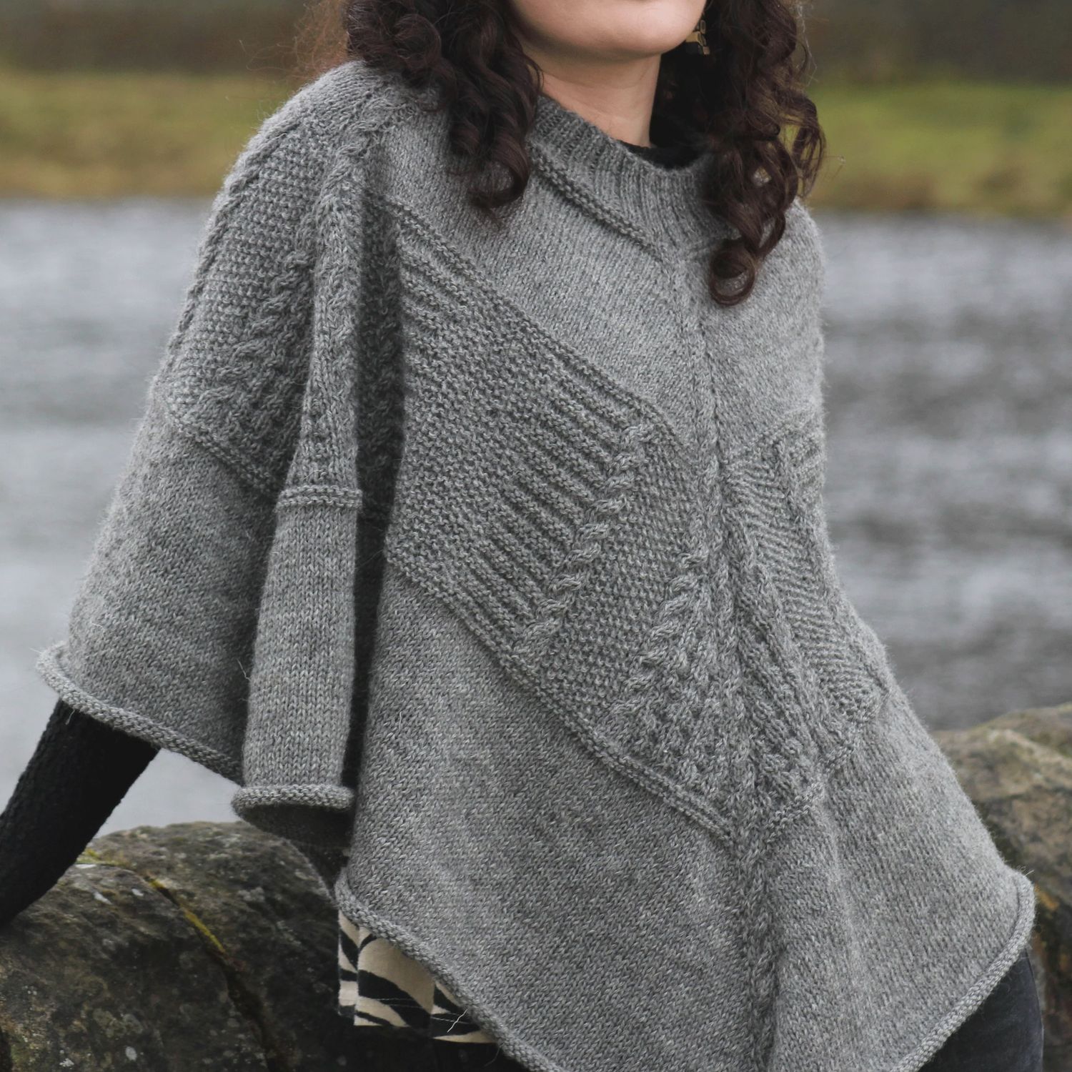 A woman is wearing a grey knitted poncho with textured sections.