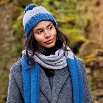 A woman is wearing a knitted had and scarf, each in 2 shades of blue.
