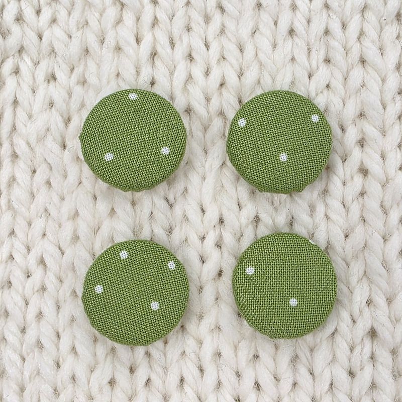 4 green fabric covered buttons with white dotty print, on a cream knitted background.