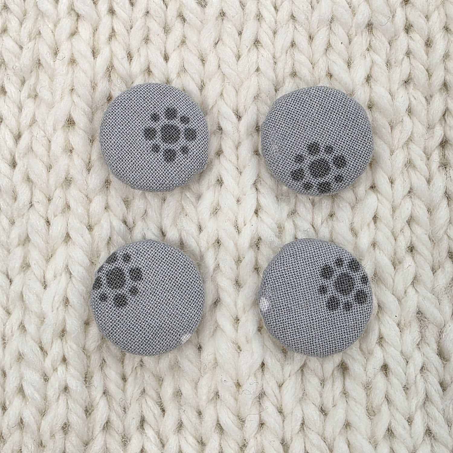 4 grey fabric covered buttons with a dark grey circular print, on a cream knitted background.
