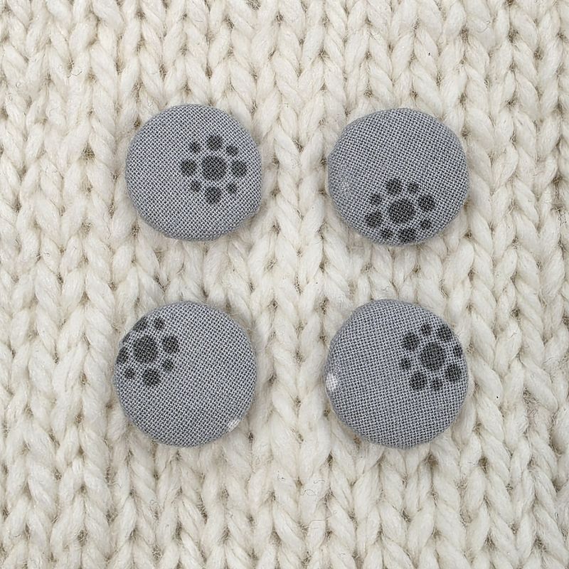 4 grey fabric covered buttons with a dark grey circular print, on a cream knitted background.