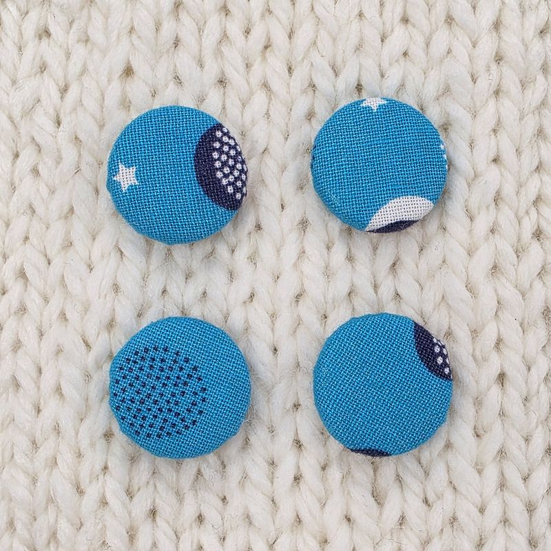 4 bright blue fabric covered buttons with white and navy blue circular print, on a cream knitted background.