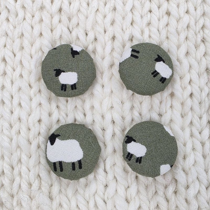 4 dark green fabric covered buttons with white sheep print, on a cream knitted background.