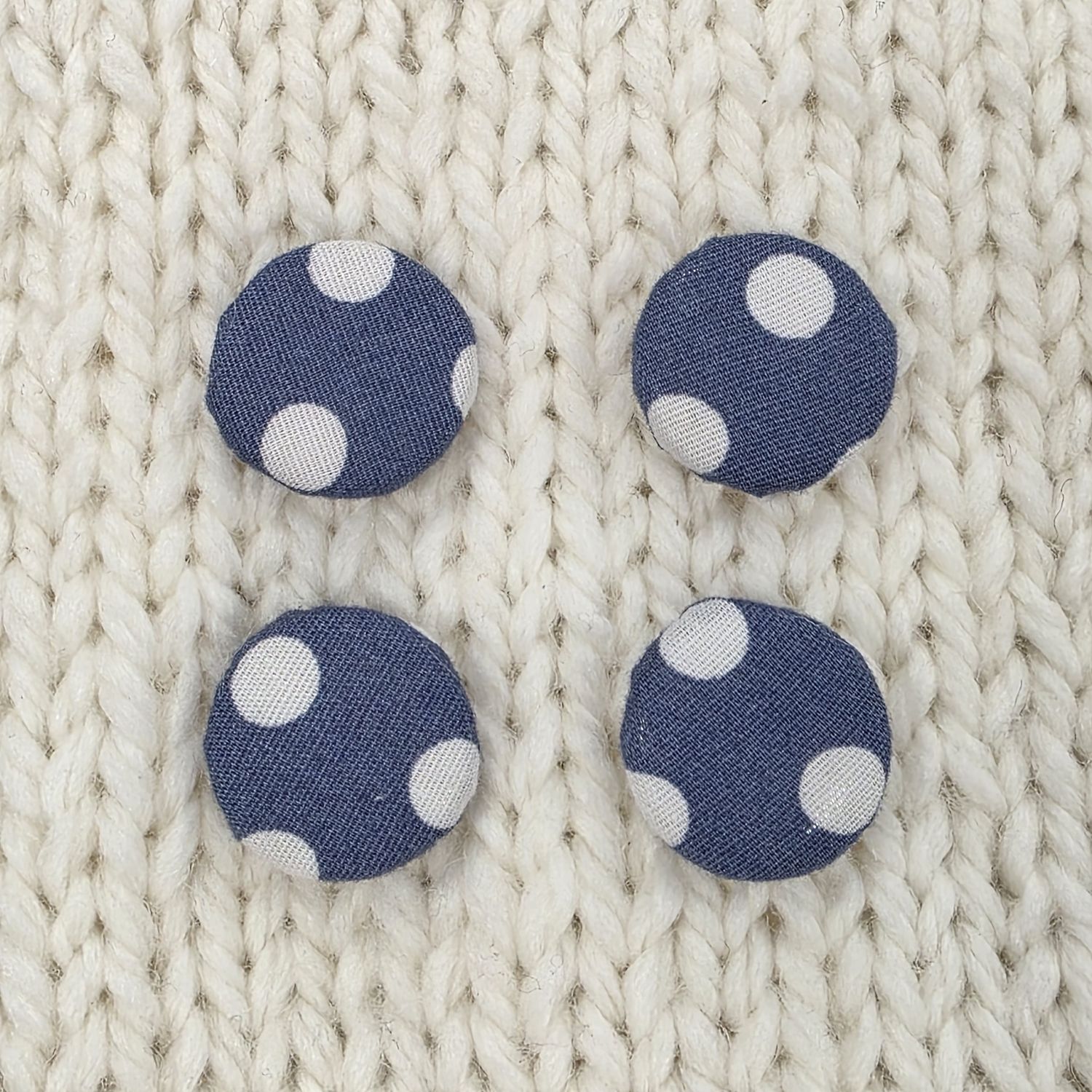 4 navy blue fabric covered buttons with white dotty print, on a cream knitted background.