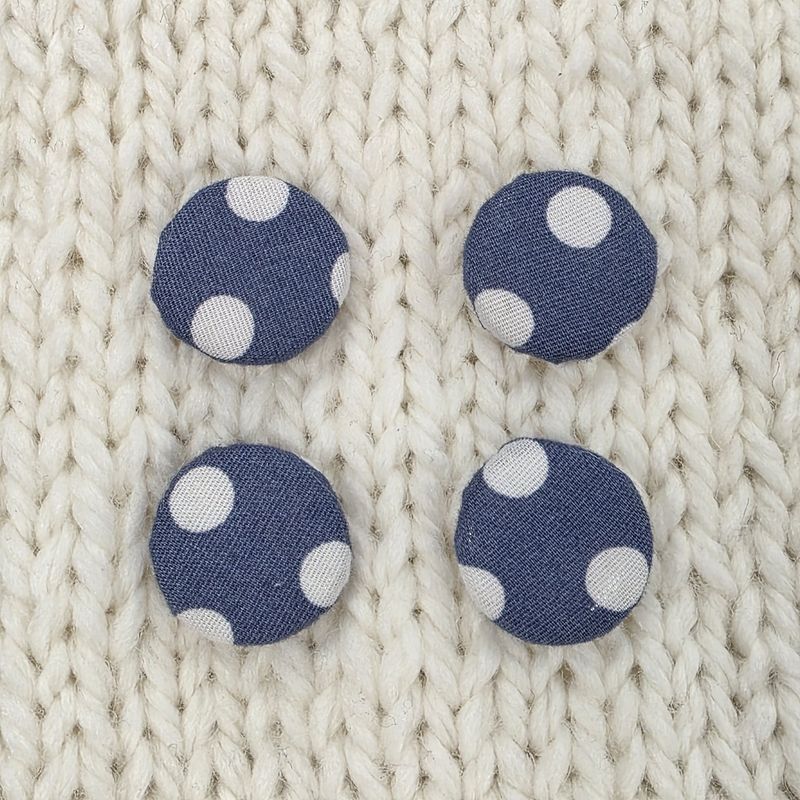 4 navy blue fabric covered buttons with white dotty print, on a cream knitted background.