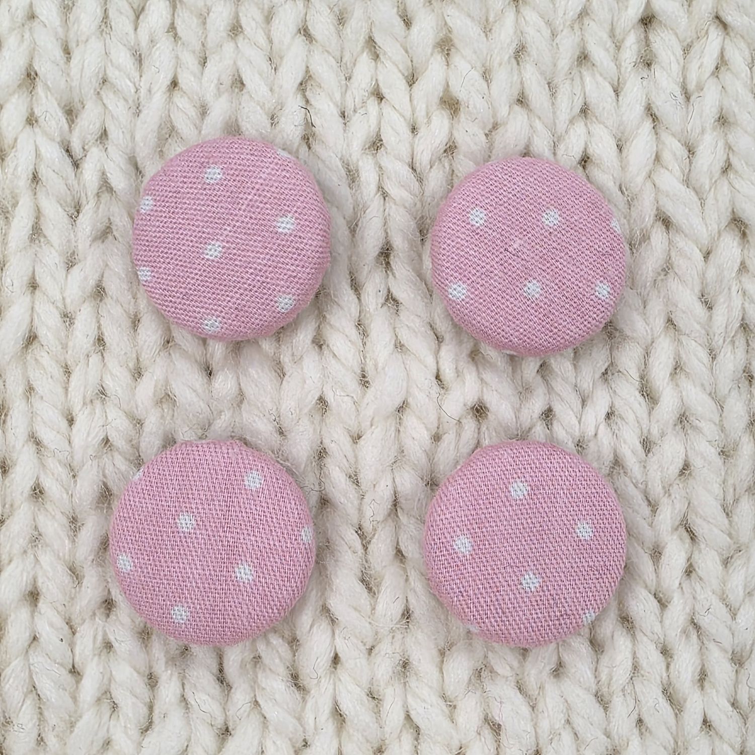 4 pink fabric covered buttons with small white dotty print, on a cream knitted background.