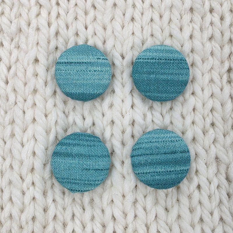 4 teal fabric covered buttons with a slight striped print, on a cream knitted background.