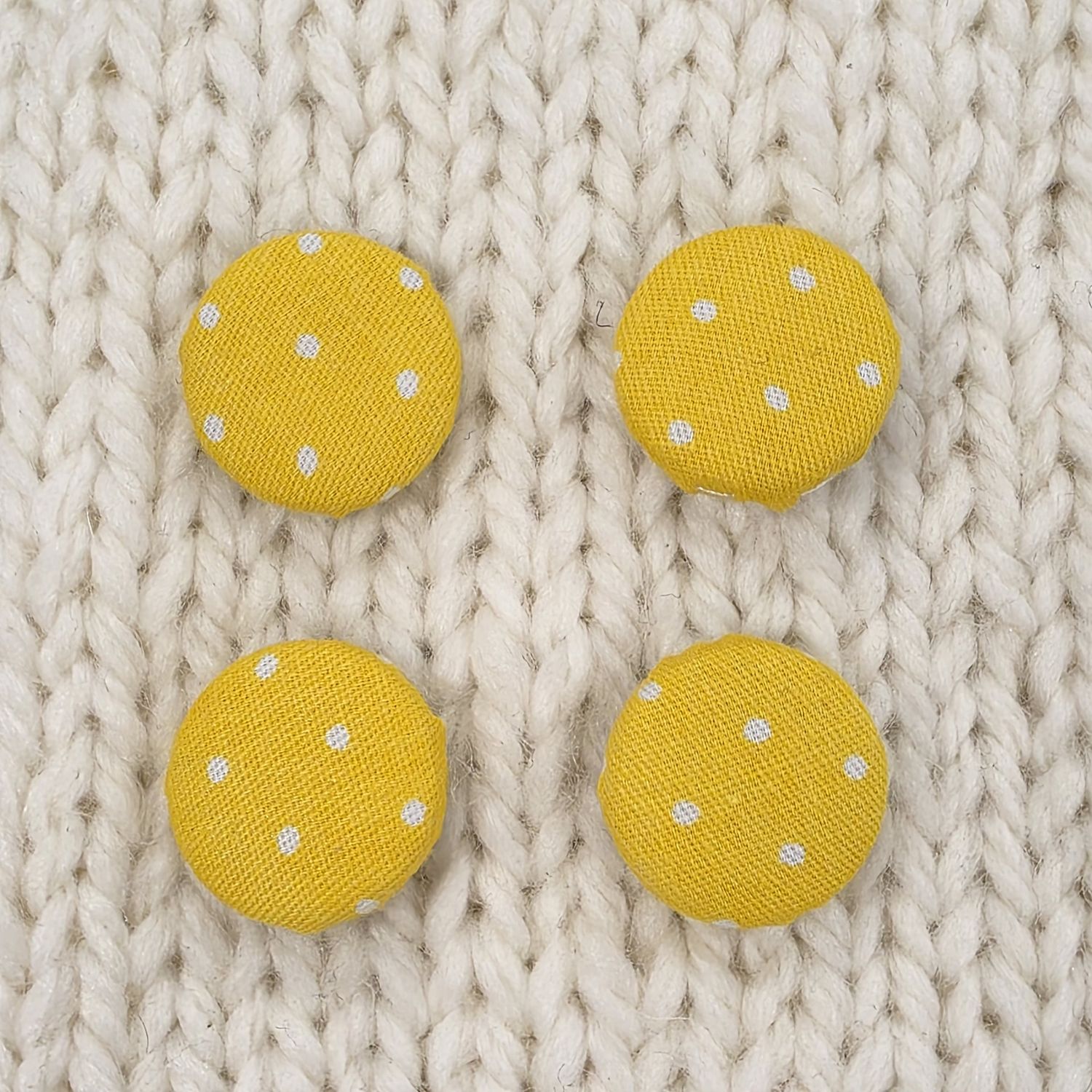 4 yellow fabric covered buttons with small white dotty print, on a cream knitted background.