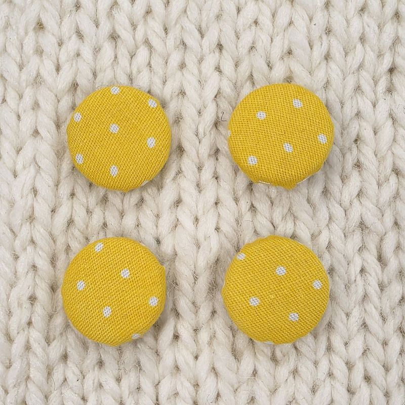 4 yellow fabric covered buttons with small white dotty print, on a cream knitted background.