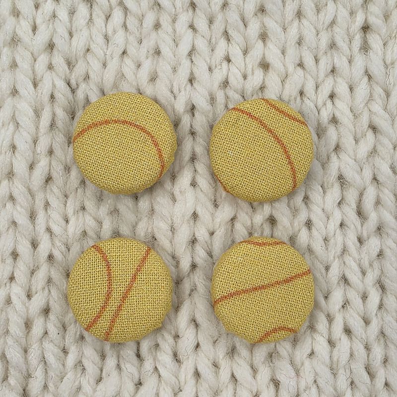 4 yellow fabric covered buttons with orange swirl print, on a cream knitted background.