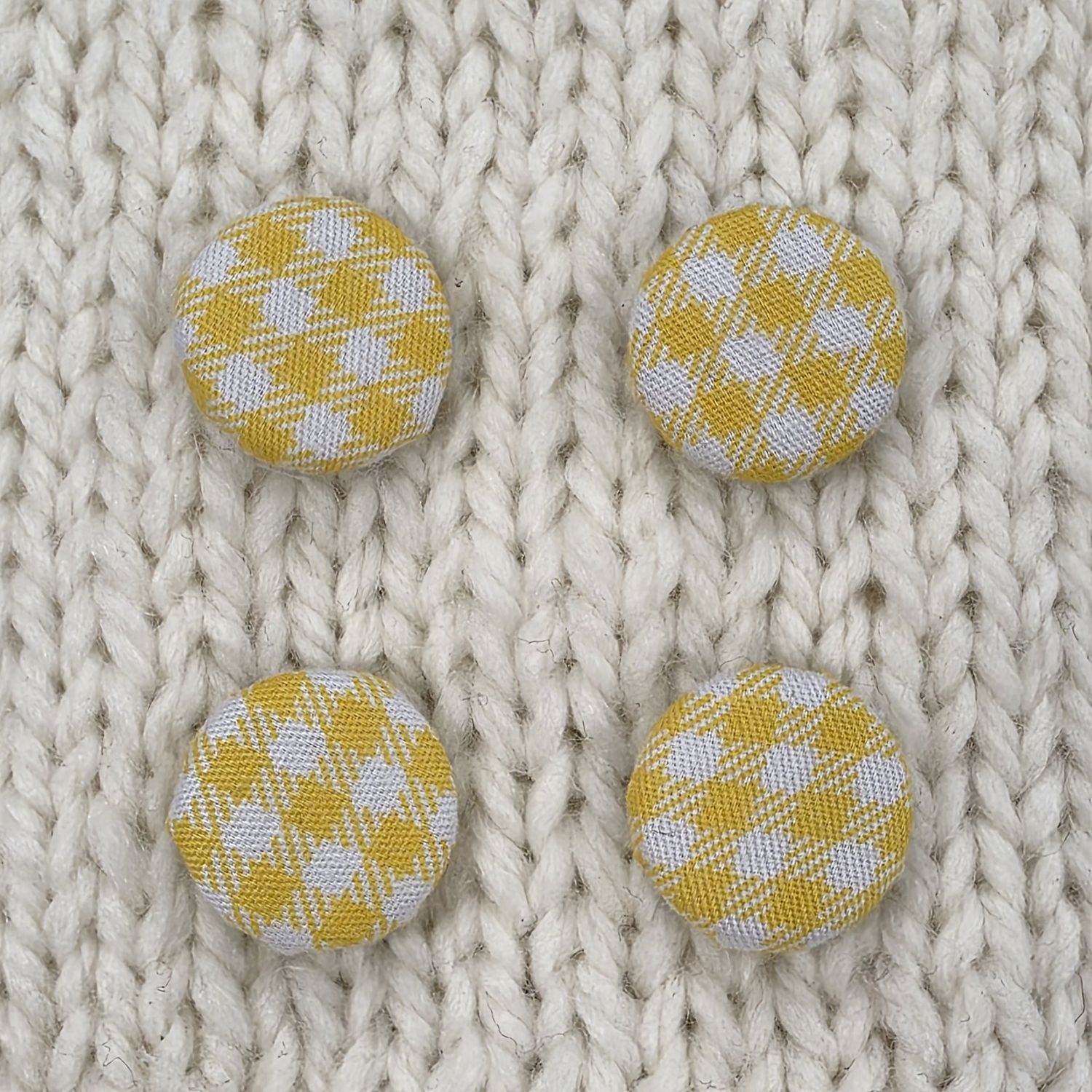 4 fabric covered buttons with a yellow and white checked print, on a cream knitted background.