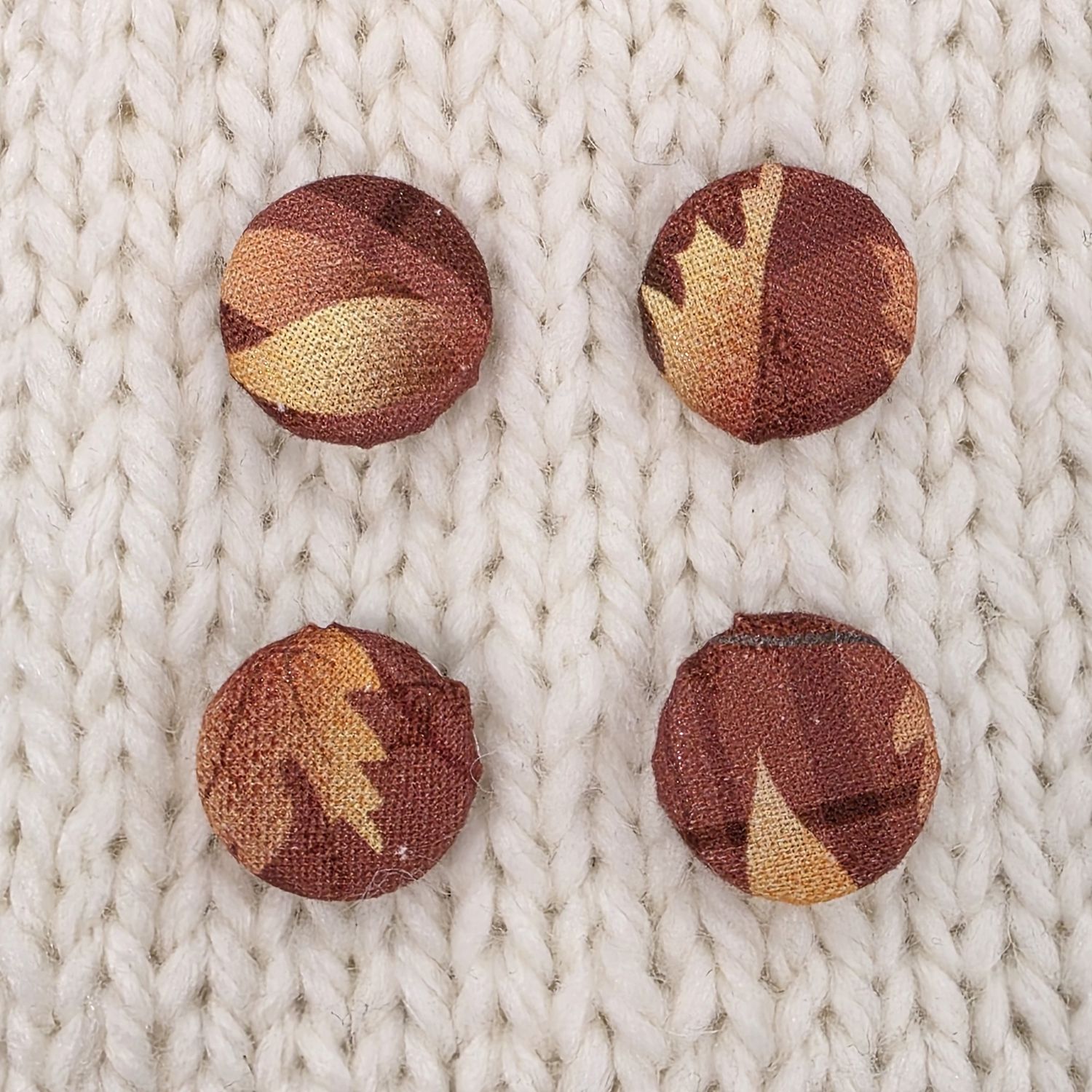 4 brown fabric covered buttons with oak leaf print, on a cream knitted background.