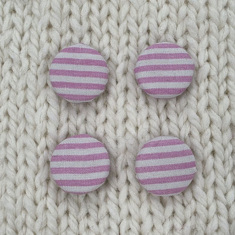 4 white fabric covered buttons with pink stripes, on a cream knitted background.