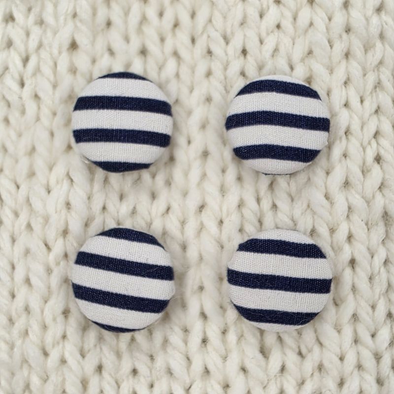 4 white fabric covered buttons with navy stripes, on a cream knitted background.