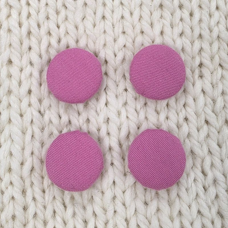 4 pink fabric covered buttons, on a cream knitted background.