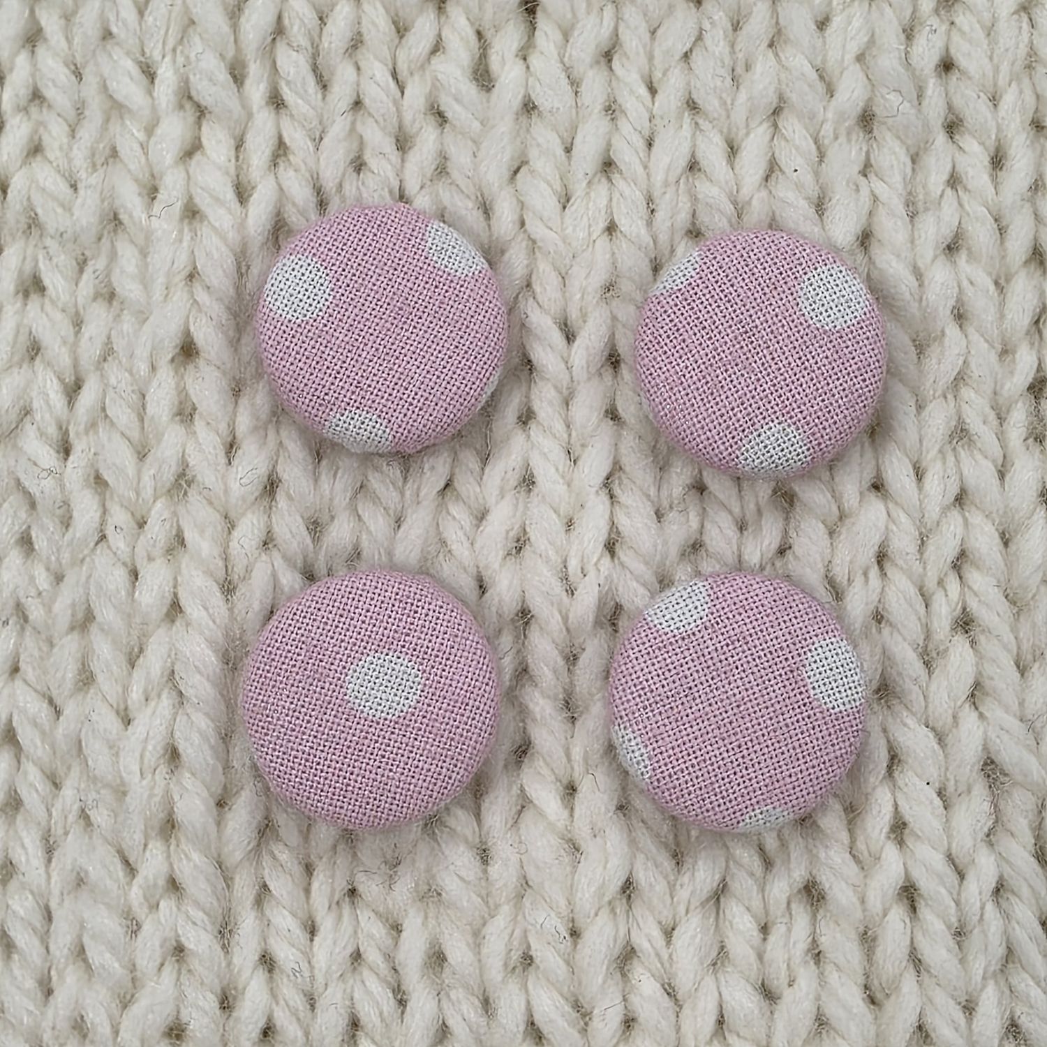 4 pink fabric covered buttons with light pink dotty print, on a cream knitted background.