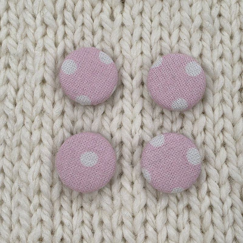 4 pink fabric covered buttons with light pink dotty print, on a cream knitted background.
