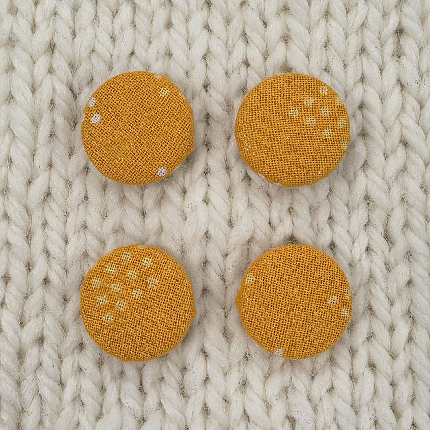 4 orange fabric covered buttons with pale orange dot print, on a cream knitted background.