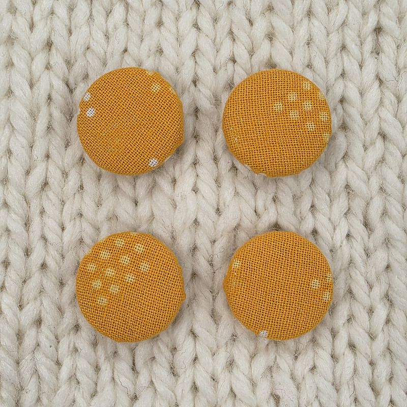 4 orange fabric covered buttons with pale orange dot print, on a cream knitted background.