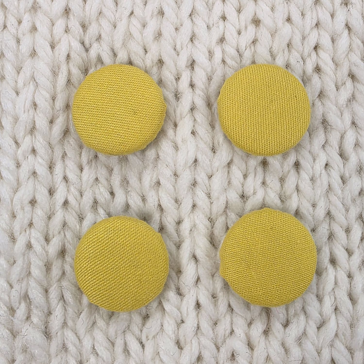 4 yellow fabric covered buttons, on a cream knitted background.