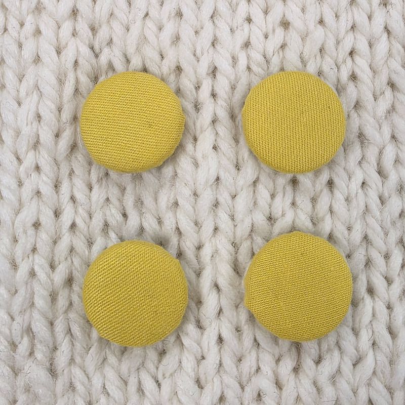 4 yellow fabric covered buttons, on a cream knitted background.