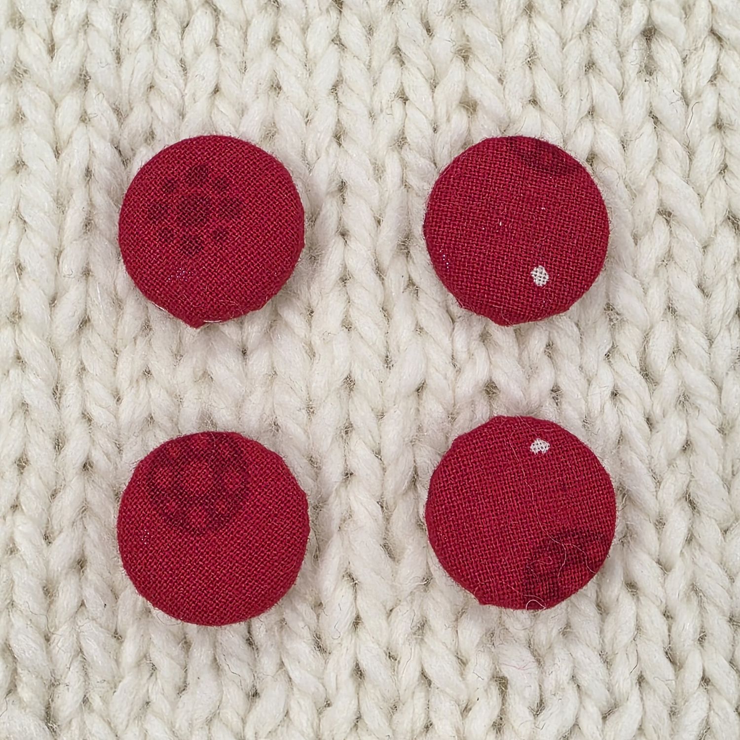 4 red fabric covered buttons with a dark red circular print, on a cream knitted background.