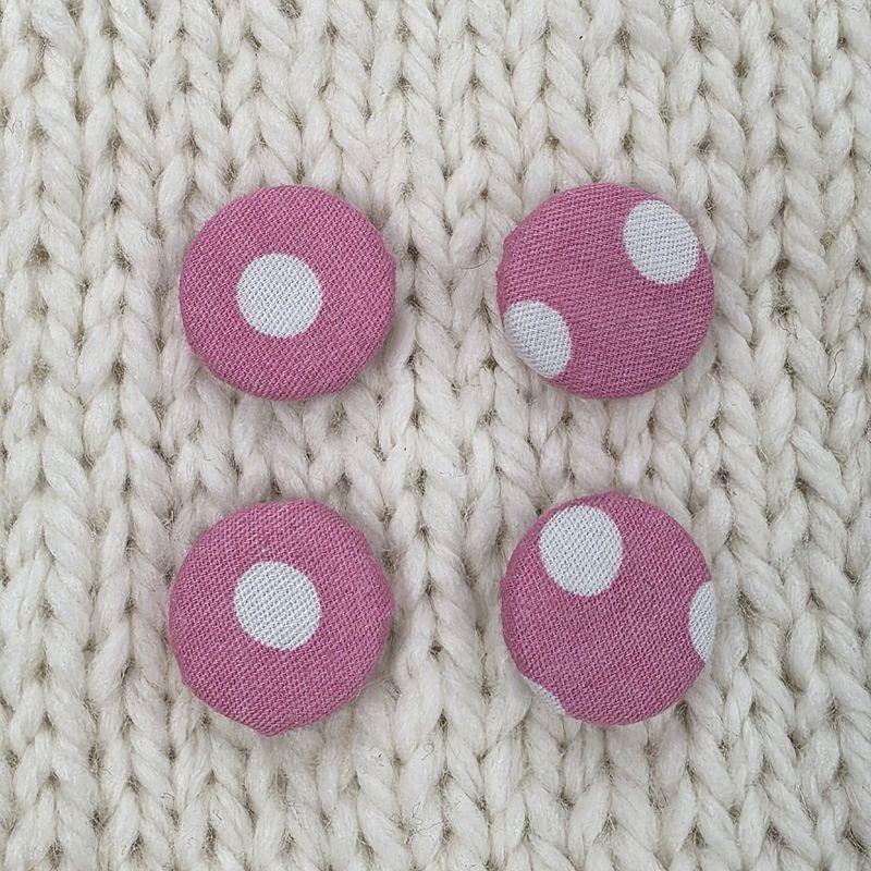4 pink fabric covered buttons with white dotty print, on a cream knitted background.