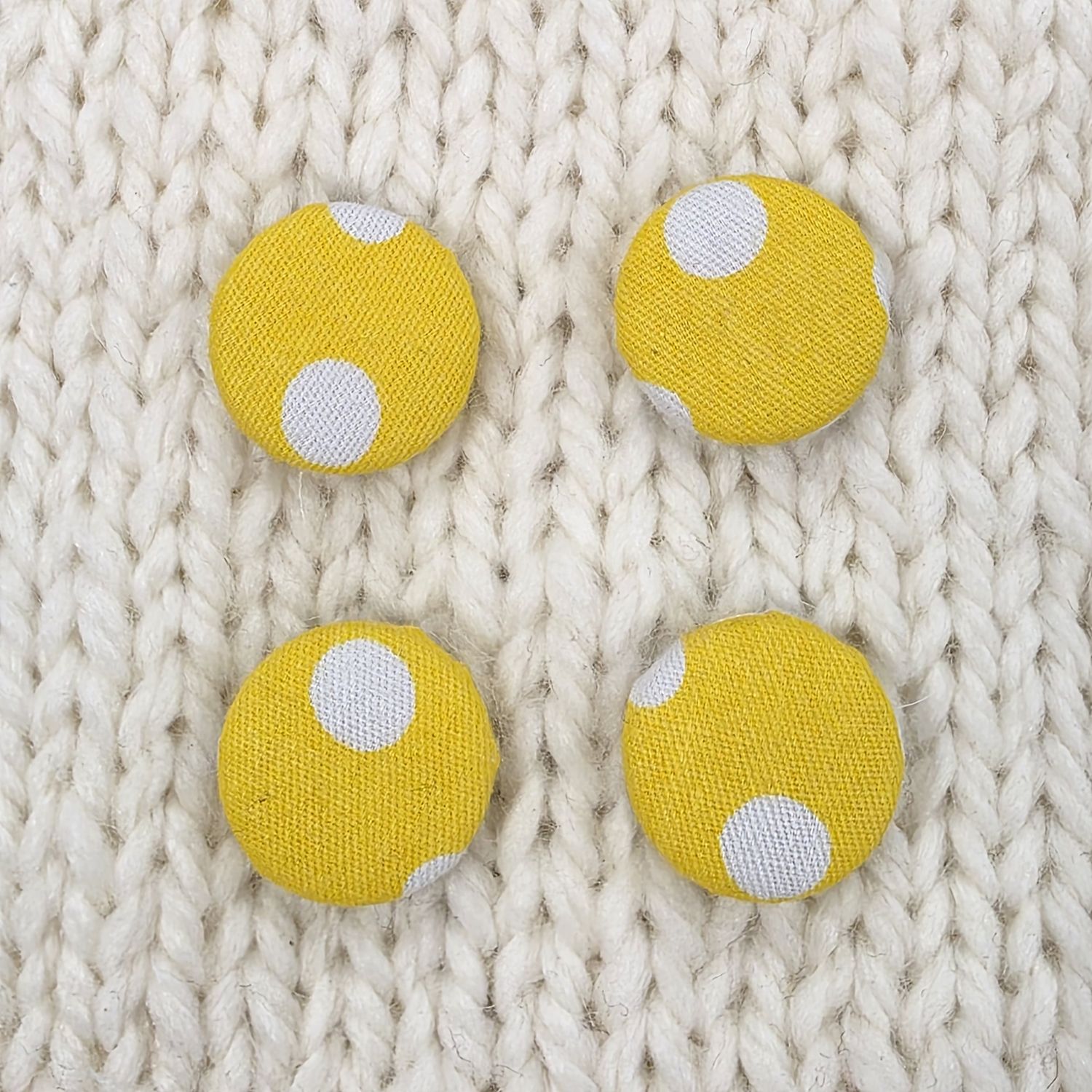 4 yellow fabric covered buttons with white dotty print, on a cream knitted background.