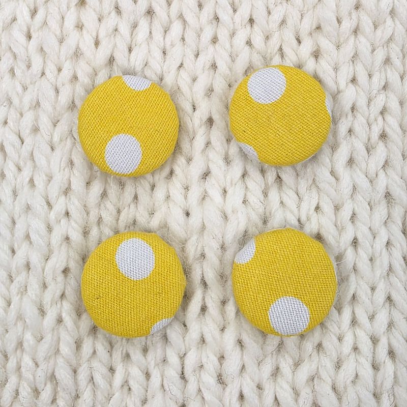 4 yellow fabric covered buttons with white dotty print, on a cream knitted background.
