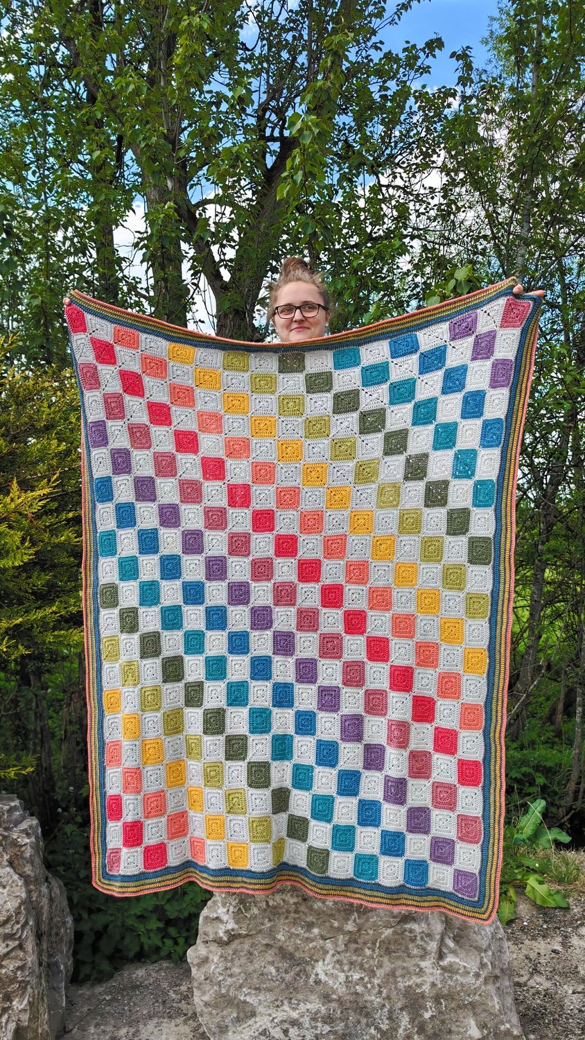 A crocheted blanket, made up of alternating light grey and rainbow squares.