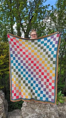 A crocheted blanket, made up of alternating light grey and rainbow squares.