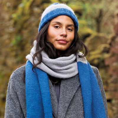 A woman is wearing a knitted hat and scarf in shades of blue and light grey.