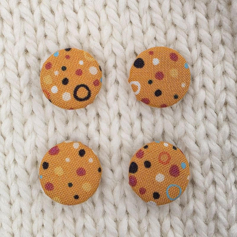 4 orange fabric covered buttons with multicoloured spots on a cream knitted background.