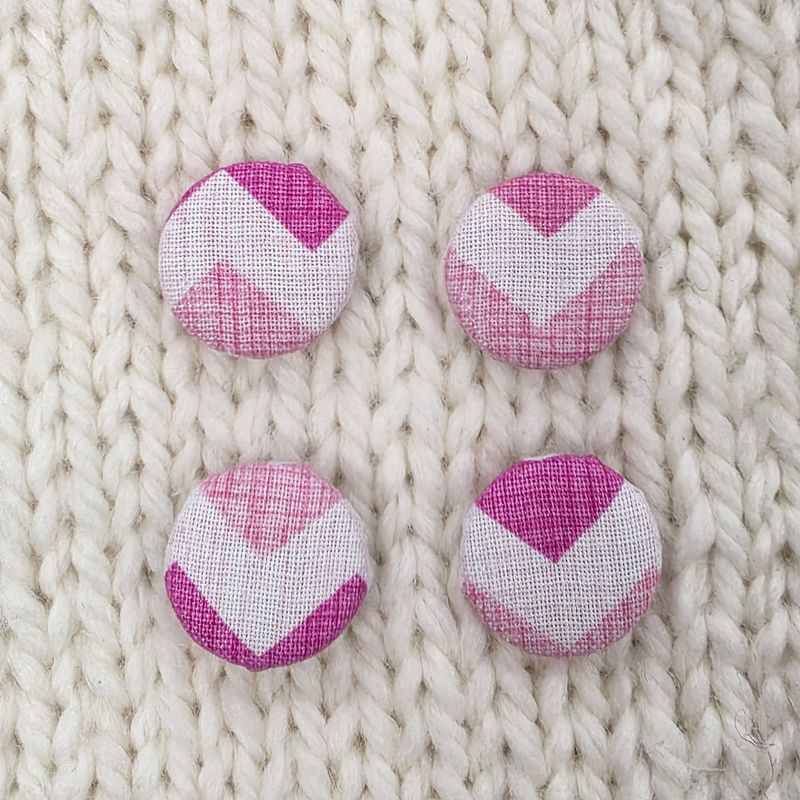 4 white fabric covered buttons with pink zig zag print, on a cream knitted background.