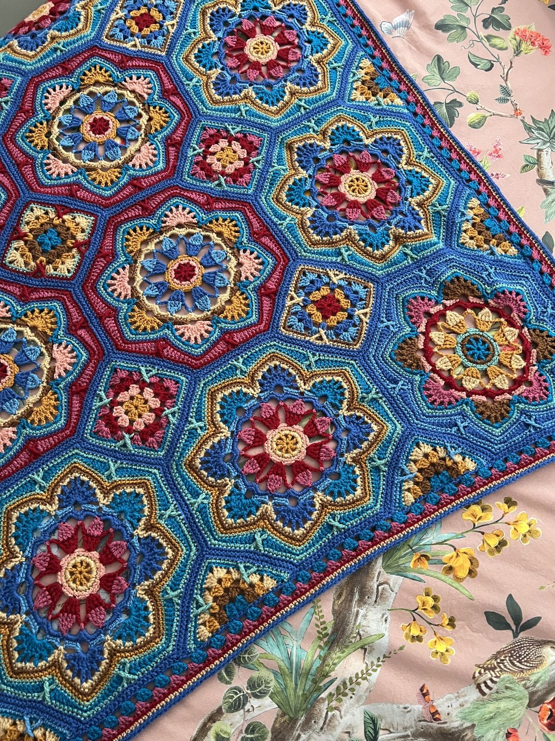 A crocheted blanket made up of octagons and squares, in shades of blues, purples and gold.