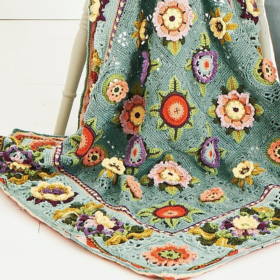 A blue crocheted blanket with colourful 3D flower motifs.