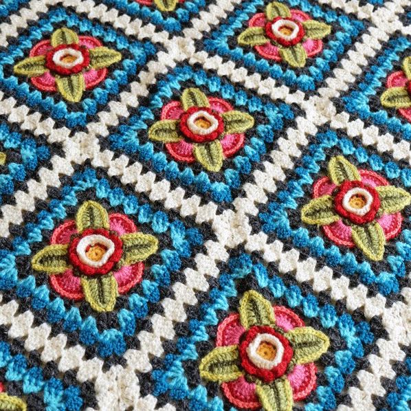 A crocheted blanket made up of blue and cream squares with pink and green flower motifs.