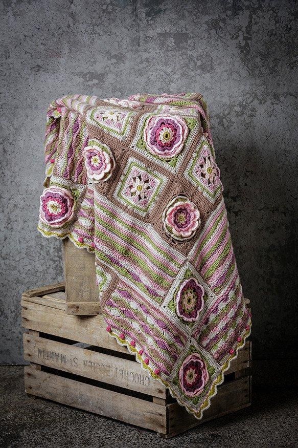A brown, pink and green crocheted blanket with 3D flower motifs.