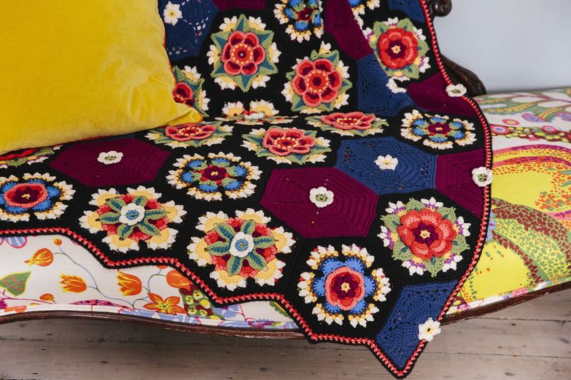 A crocheted blanket made up of crocheted hexagons in dark red, navy blue, black and small amounts of lighter shades.