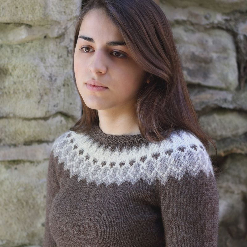 A woman is wearing a brown knitted sweater with cream colourwork around the yoke.