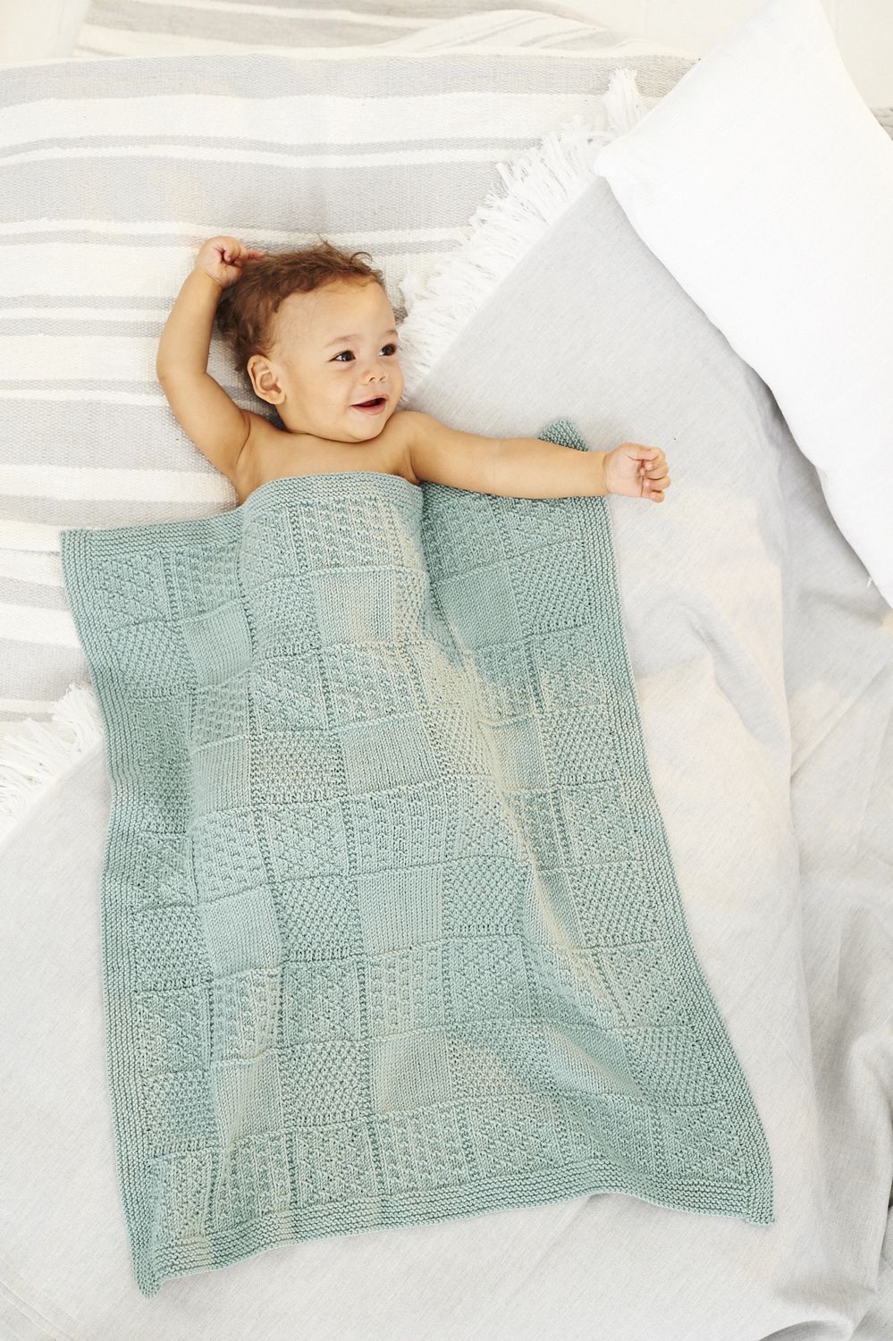 A baby is laid under a sage green knitted blanket.