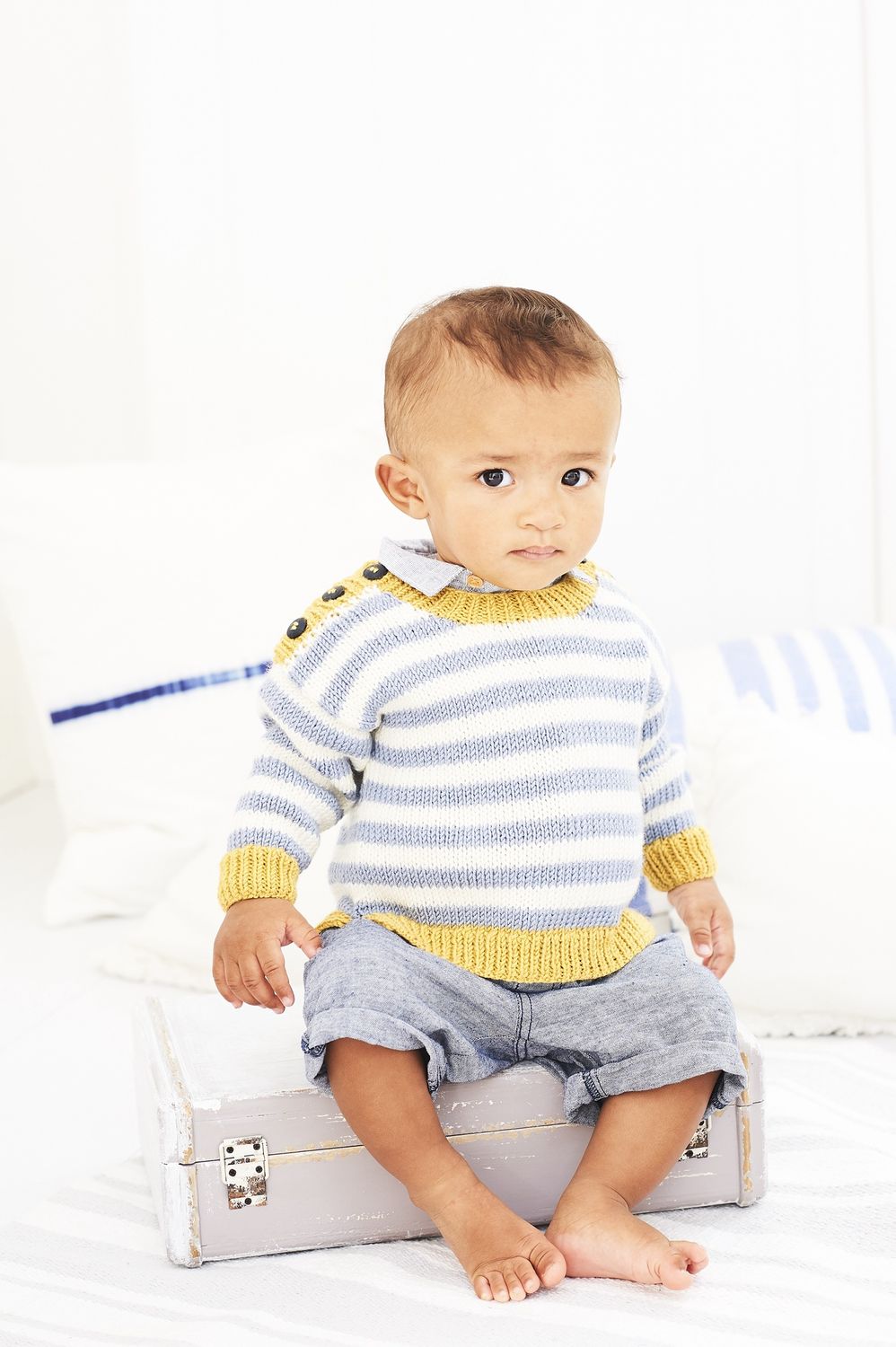 A baby is wearing a white and grey striped knitted sweater with yellow trim.