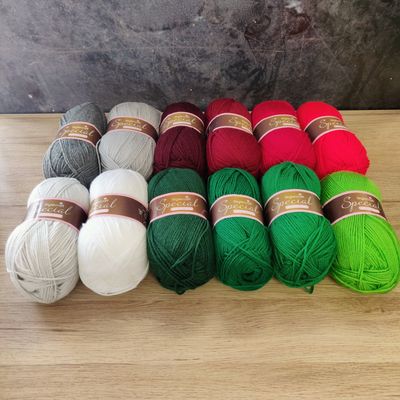 12 balls of yarn in shades of grey, white, red and green laid out on a wooden surface.