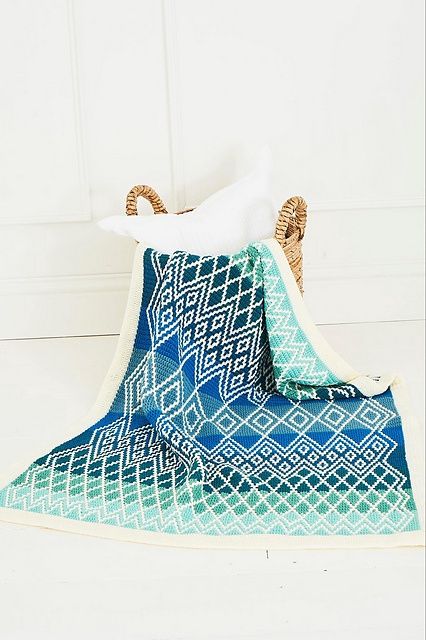 A crocheted blanket in various shades of blue, with a cream diamond shaped design.