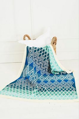 A crocheted blanket in various shades of blue, with a cream diamond shaped design.