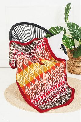 A crocheted blanket in various shades of red and orange, with a cream diamond shaped design.